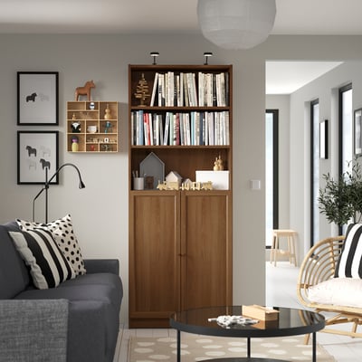 Cosy living room with BILLY bookcase & dark couch. Books, decor, & lamp on shelves; wall art, trinkets, & coffee table.