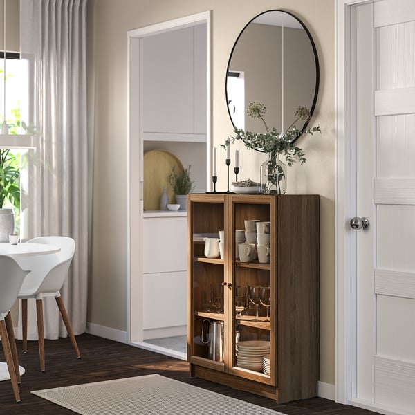 Modern living room with BILLY brown cabinet, glass doors, adjustable shelves, black mirror, and flower vase.