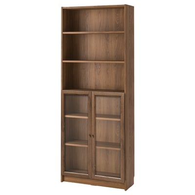 This image displays a wooden BILLY bookcase in brown with glass doors, featuring multiple shelves for storage.