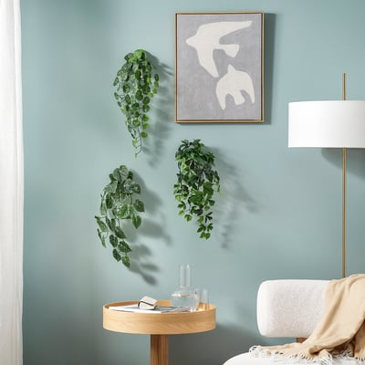 Green FEJKA wall plants, minimalist painting, soft lighting, cosy chair.