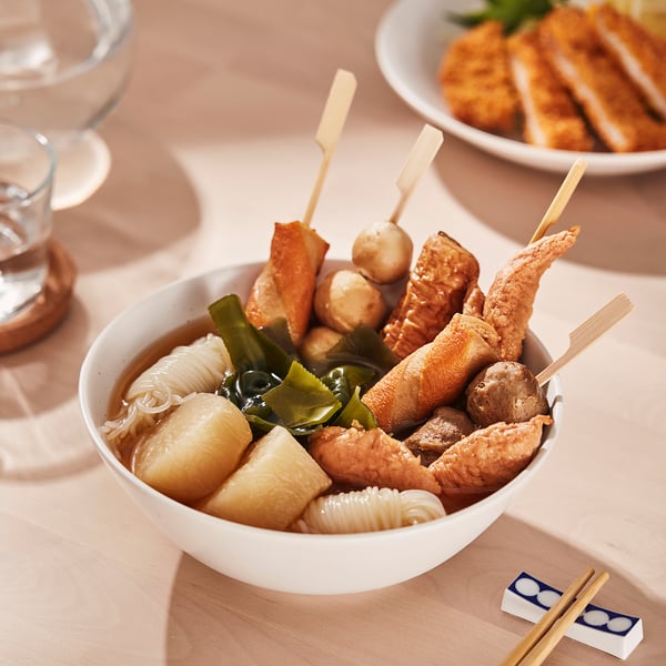A bowl of assorted skewered foods and noodles in broth, with chopsticks nearby.