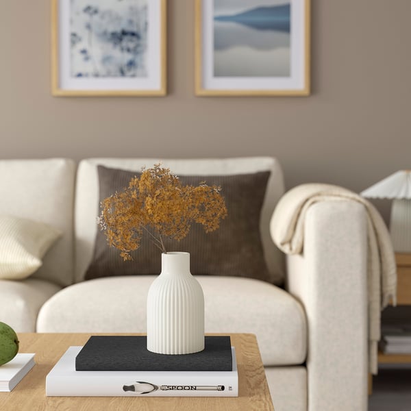 Modern living room with KAPKASTANJ vase on coffee table, yellow flowers, beige couch, and nature paintings.