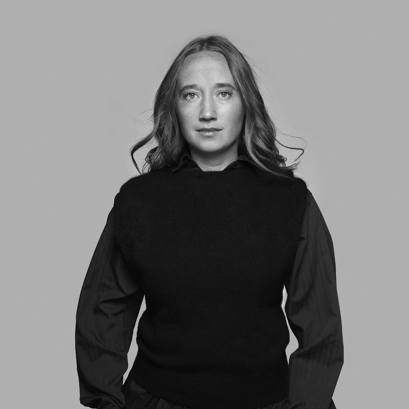 Black and white portrait of the designer with long hair, posing confidently.