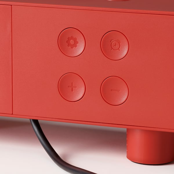Red clock with circular buttons: gear, alarm, plus, minus. Elevated design, modern functionality.