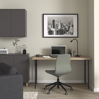Modern home office with LAGKAPTEN desk, laptop, lamp, cityscape art, grey storage, sofa, light green chair.