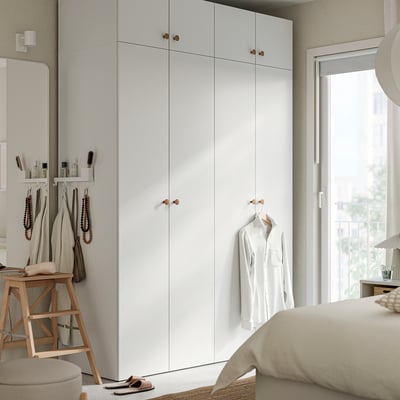 Modern bedroom with large white LASTARE wardrobe, wooden knobs, alongside bed with beige bedding and hanging shirt.