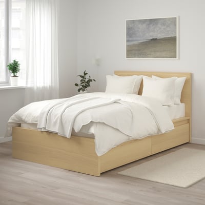 Minimalist bedroom with light wooden MALM bed, white linens, art on wall, and plants. Bed is large, fitting neatly under a window.