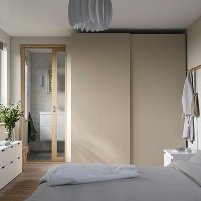 Modern bedroom large beige PAX wardrobe, white pendant light, and neat bed linens with bathroom view.