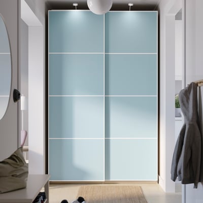 A modern white and light blue sliding closet with a large mirror, occupying a wide space in a well-lit room.
