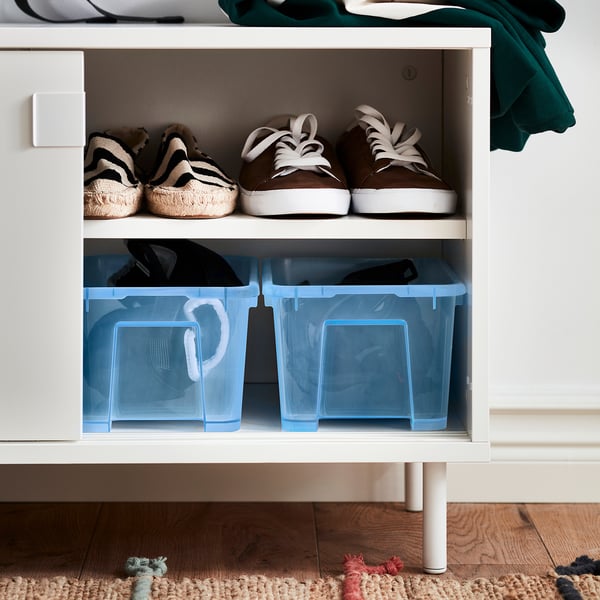 White cabinet with two shelves: two blue bins, striped sandals, brown trainers.