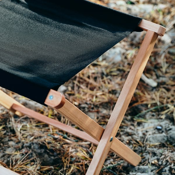 Close-up of a black canvas foldable stool with sturdy wooden legs.