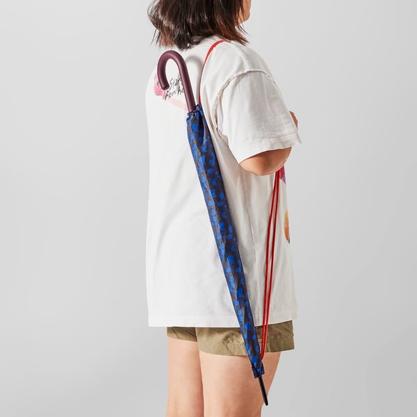 Person holding colourful polka-dot umbrella over shoulder, wearing a white t-shirt with heart design.