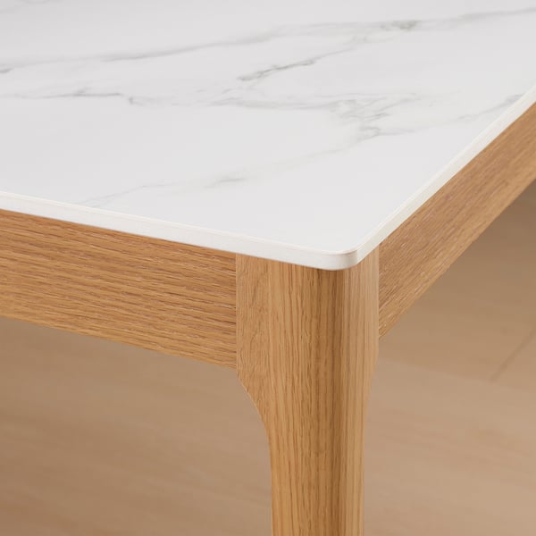 A sleek dining table with a smooth, white ceramic top featuring subtle veining and sturdy wooden legs.