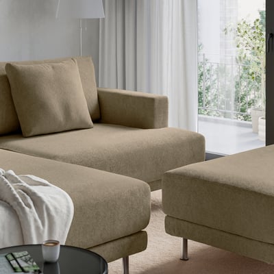 Modern beige sofa with cushions and blanket, next to a table with a cup.