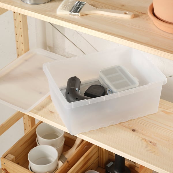 Wooden shelves with clear UPPSNOFSAD plastic box holding small black items. Box is larger than white cups below it.