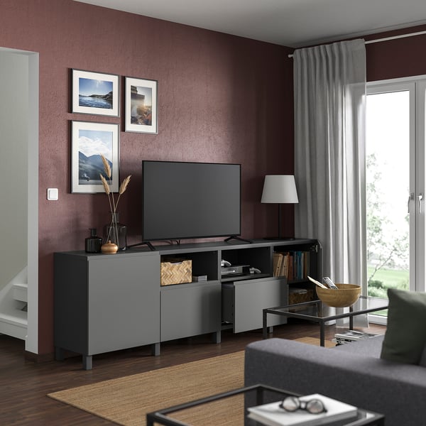 Sodobna dnevna soba z kostanjevo steno, TV BESTÅ, TV z ravnim zaslonom, črne vaze, uokvirjena umetnost, siva preproga, steklena miza, lesena skleda.