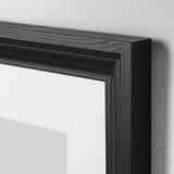 Črni okvir za slike z elegantnimi, gladkimi robovi, naslonjenimi na navadno steno. Visokokakovostna zasnova, ki prikazuje robustno konstrukcijo in sodobno estetiko.