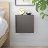 Minimalistična spalnica s temno sivo omarico EKET, rastlino in uro.