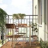 Balkon z akacijevim lesom FURUÖN in belo kovinsko jedilno garnituro; Vključuje mizo, stole in podnožje. Obkrožen z lončnicami, ki ustvarjajo prijeten prostor.