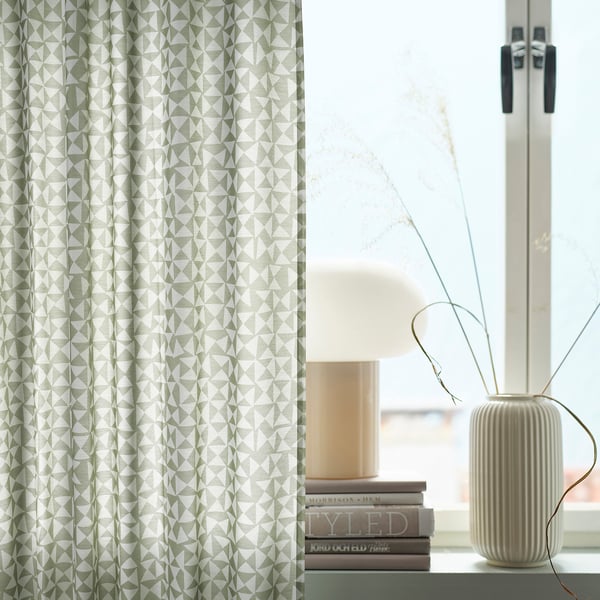 Sodobna soba z zeleno-belimi geometrijskimi zavesami HÅRKÖRVEL, elegantno okensko polico, svetilko, knjigami in minimalističnim dekorjem.
