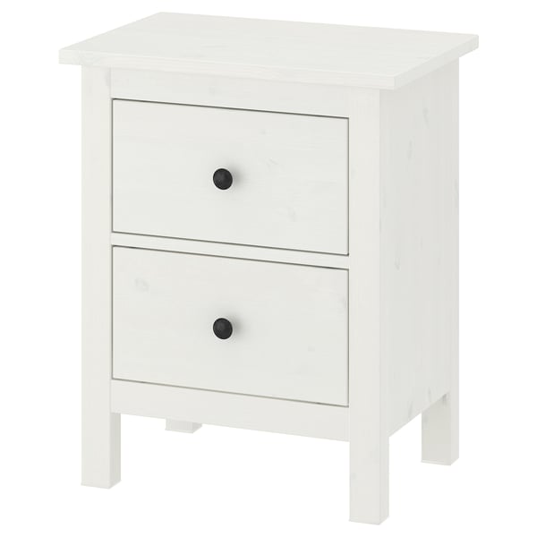 Bela lesena komoda HEMNES z dvema predaloma, od katerih ima vsak črne gumbe, stoji na štirih nogah.