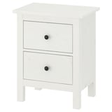 Bela lesena komoda HEMNES z dvema predaloma, od katerih ima vsak črne gumbe, stoji na štirih nogah.