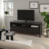 HEMNES črno-rjavo stojalo za TV s policami in predali, držalno TV, med mizami in rastlino.