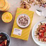 Ikea HJÄLTEROLL škatla za granola z oreščki in jagodami. Odprta škatla prikazuje mešanico granole, pripravljeno za uživanje z jogurtom in sadjem.