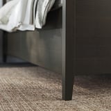 Temno rjav okvir postelje IDANÄS z elegantnimi nogami in belo posteljnino, ki prikazuje sodoben dizajn.