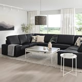 Moderna dnevna soba z velikim črnim kavčem KIVIK v obliki črke L, belo mizico in velikim oknom, ki ponuja udoben in eleganten prostor.