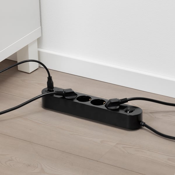Črna napajalna palica z več vtičnicami na lesenih tleh z USB priključki za polnjenje naprav.