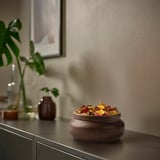 Zemeljsko rjava lončena posoda MÄVINN na črni mizi, minimalističen dizajn.