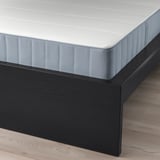 Bližnji posnetek črnega lesenega posteljnega okvirja z belo prešito vzmetnico, ki prikazuje njegovo elegantno obliko in podporno strukturo.