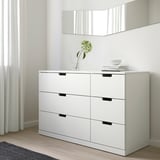 Ikea NORDLI 6-predalna komoda ob steni, minimalistična soba, vaza z zeleno rožo, knjige.