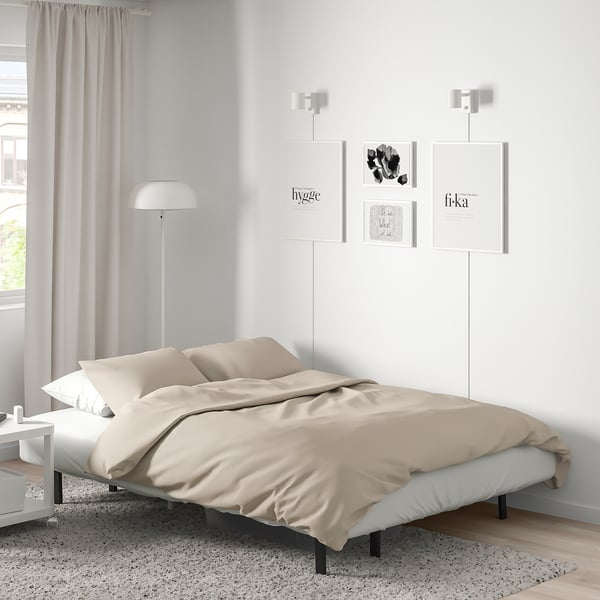 Sodobna minimalistična spalnica z bež posteljo, sivimi zavesami, umetniškimi deli in talno svetilko.