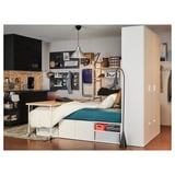 Majhna spalnica z belo posteljo PLATSA, črnimi omarami, zeleno odejo, leseno mizo in visečo svetilko.