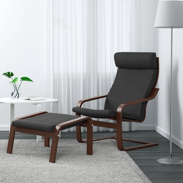 Stol Ikea POÄNG, temno siva, s podnožjem, svetilko, stransko mizico in rastlino na preprogi.