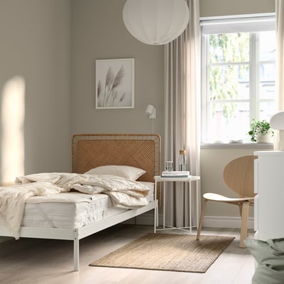 Udobna spalnica z belo posteljnino, RÅDHUSVIN ščitnikom, lesenim vzglavjem, svetilko, stolom, oknom, knjigami, rastlino.