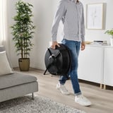 Oseba, ki nosi črni čistilec zraka z ročajem v sodobni dnevni sobi. Proizvod: STARKVIND.