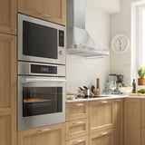 Sodobna kuhinja z dvojno pečico iz nerjavečega jekla in mikrovalovno pečico iz IKEA. Eleganten, funkcionalen dizajn z digitalnimi kontrolami in možnostjo zračnega cvrtja.