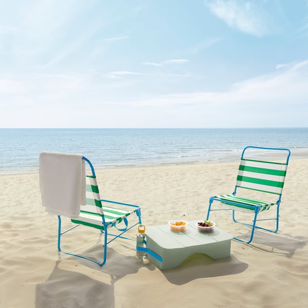 Dva zeleno-bela črtasta ležalnika za plažo STRANDÖN z majhno belo mizico na peščeni plaži, ocean v ozadju.