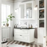 Elegantna bela umivalnica TÄNNFORSEN z okroglim umivalnikom, ogledalnimi omarami in kariranimi tlemi.
