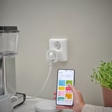 Oseba drži pametni telefon, ki upravlja vtič, povezan z aparatom za kavo prek aplikacije za pametni dom, kar prikazuje daljinsko upravljanje naprav.