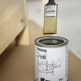 Krtač, namočen v lesno olje TRIXIG, pripravljen za nanos, na pločevinki pa je prikazano ime izdelka, uporaba in čas sušenja.