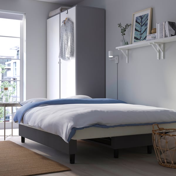 Moderná spálňa s modrou posteľnou bielizňou, rámami na obrazy a prirodzeným svetlom.