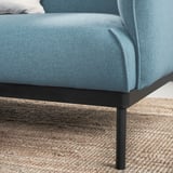 Modrá čalúnená pohovka s kovovými nohami na jutovom koberci.