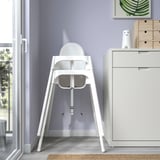 Biela vysoká stolička proti fialovej stene, ľahko sa montuje/rozoberá. Bezpečnostný pás je súčasťou balenia.