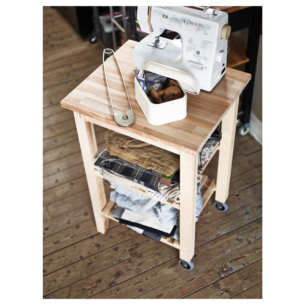 Drevený šijací vozík s bielym strojom, náradím a látkou.