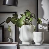 Biela keramická váza so zelenou rastlinou; umiestnené na stohu kníh; čistý, moderný dekor.