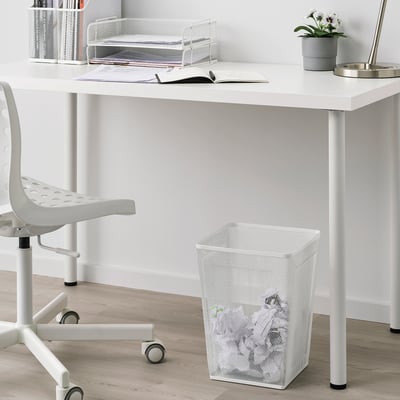 Biely kovový kôš na papier pod stolom vedľa stoličky. Jednoduchý moderný dizajn. Menšie ako stolička a stôl.